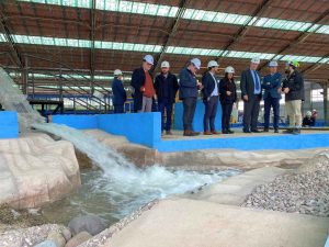 Personas de pie sobre la estructura que representa el modelo físico del embalse Ancoa, con agua.